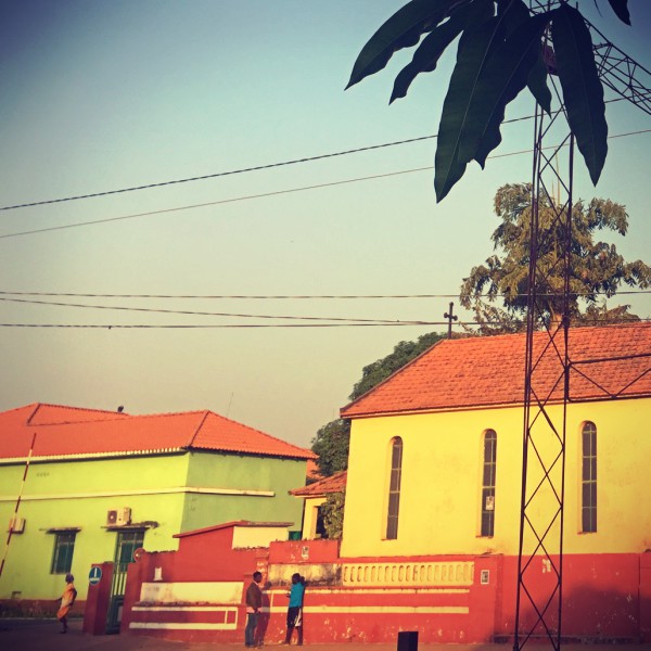 Trois personnes dans une rue de Bissau, bâtiments verts, jaunes et ocres #Off2África 50 Bissau Guinée-Bissao © Gilles Denizot 2017