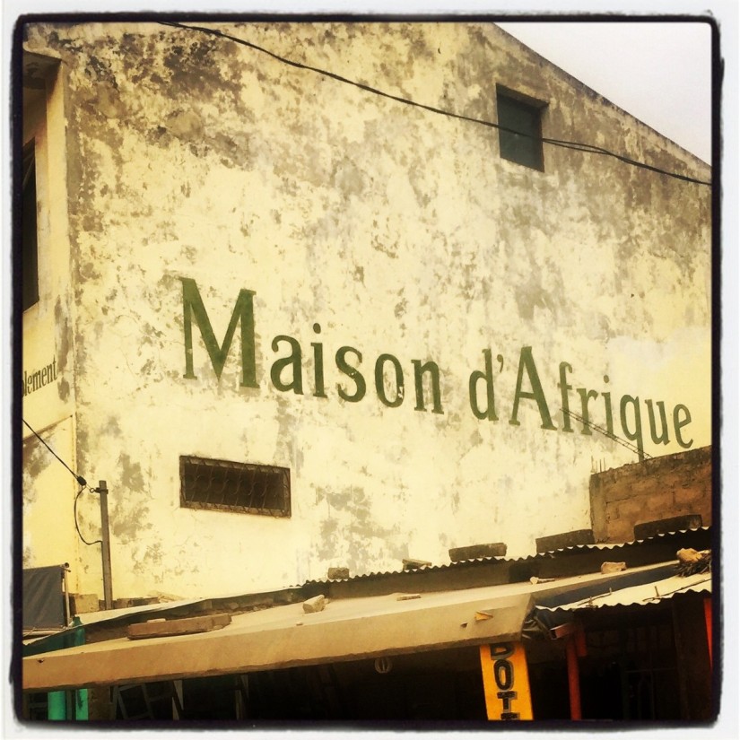 Une grande maison de couleur jaune. Sur la façade, il est écrit en lettres vertes : Maison d'Afrique #Off2Africa 33 Mbour Sénégal © Gilles Denizot 2016