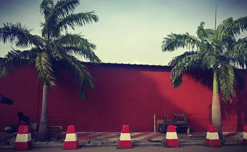 Un grand mur rouge, deux palmiers de chaque côté, un trottoir rouge et blanc et des blocs rouges et blancs #Off2Africa 97 Abidjan Côte d'Ivoire © Gilles Denizot 2017