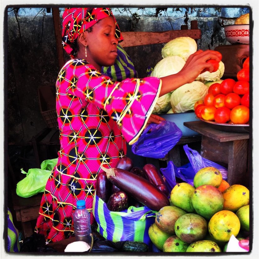 Une marchande de fruits et légumes vêtue d'un boubou rose dispose des tomates sur un plat #Off2Africa 70 Conakry Guinée © Gilles Denizot 2017