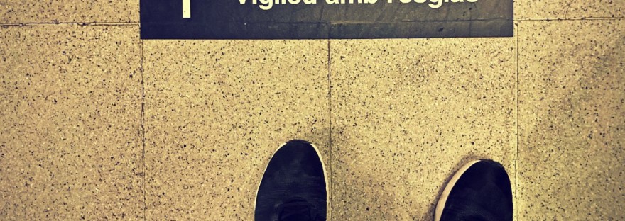 Vue d'en haut sur chaussures de sport noires et un avertissement en catalan. Lignes obliques jaunes et noires. #HolaBarcelona juillet 2023 © Gilles Denizot