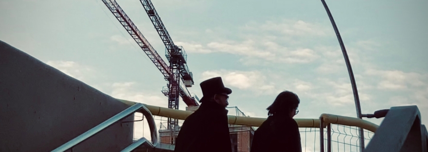 Barcelone, un homme vêtu d'un cape et coiffé d'un haut-de-forme, et une femme vêtue de noir se profilent contre le ciel, les grues, un réverbère #HolaBCN Quand les douze coups de minuit © Gilles Denizot 2023