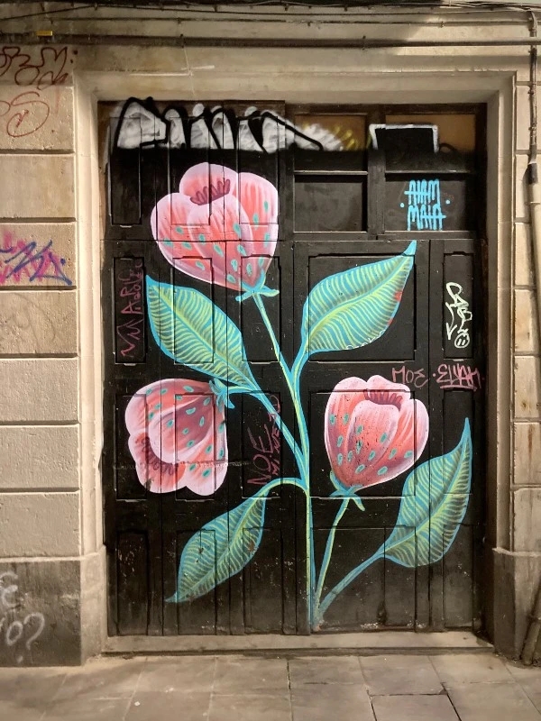 Une porte de Barcelone sur laquelle a été peinte une branche et trois fleurs roses #HolaBCN Voleur de sable © Gilles Denizot 2024
