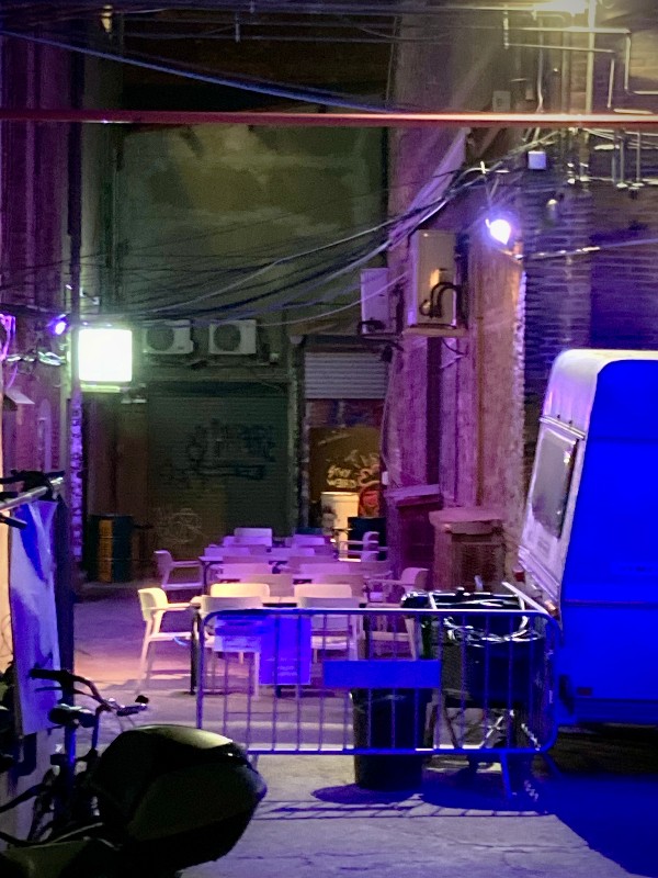 Grand foutoir typique de l'entrée de mon immeuble. Tables, chaises, néons, lumière violette et même une caravane #HolaBCN thankyouforthehappy © Gilles Denizot 2024
