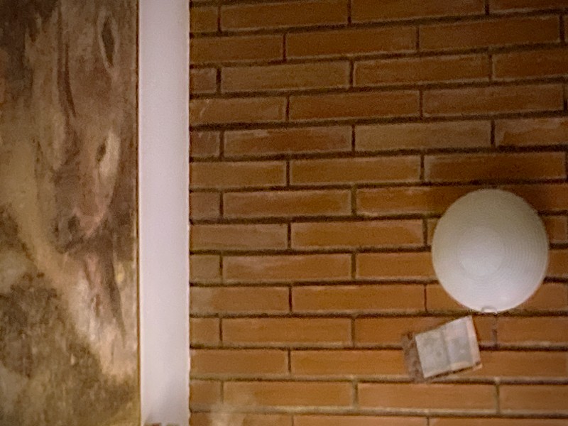 Détail d'un mur en briques, à gauche un tableau, à droite une lampe et une carte postale #HolaBCN Le vieux quartier © Gilles Denizot 2024
