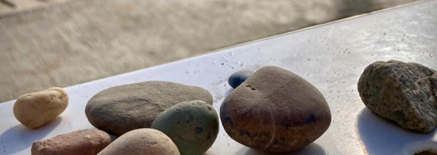 Des galets sur un banc en pierre, des grains de sables, et la base des douches sur une plage de Barcelone #HolaBCN Voleur de sable © Gilles Denizot 2024