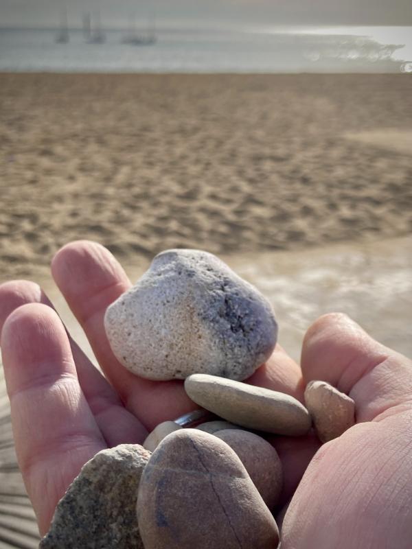 Ma main tenant des galets, au loin le sable et la mer #HolaBCN Voleur de sable © Gilles Denizot 2024