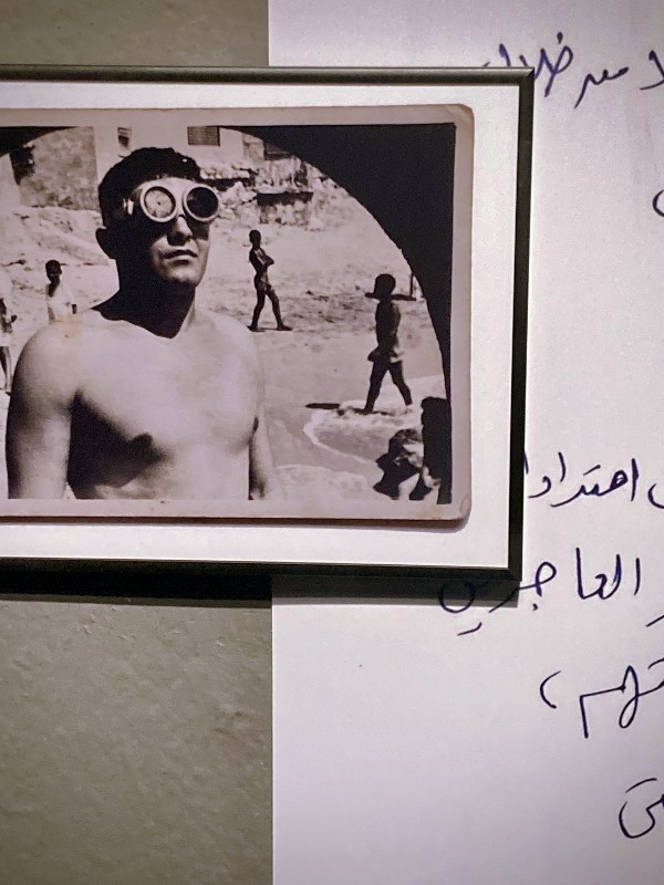 Photo ancienne d'un homme portant des lunettes de plongée, derrière un fragment de texte en arabe #HolaBCN Le vieux quartier © Gilles Denizot 2024