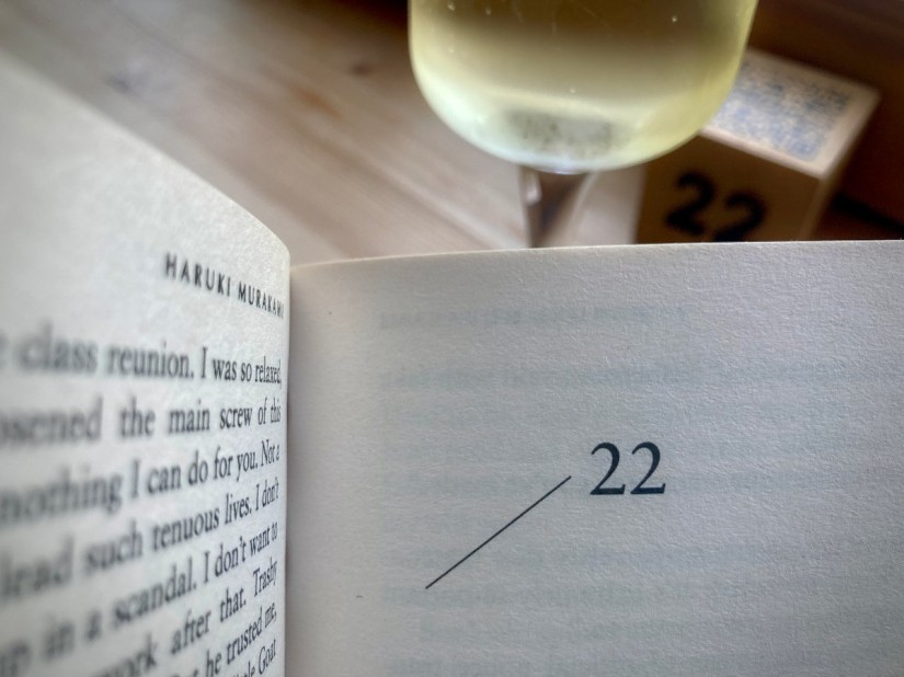 Un livre de Haruki Murakami ouvert au chapitre 22. En second plan, une coupe de cava et un cube qui indique 22 #HolaBCN Galaxie cinq sept © Gilles Denizot 2024